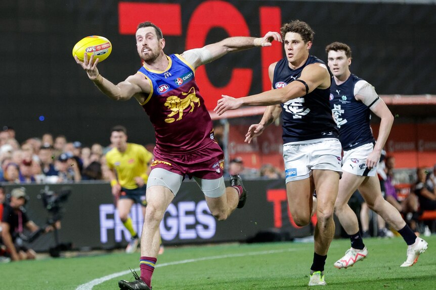 Darcy Gardiner holds the ball in one hand near the boundary line as Charlie Curnow chases him