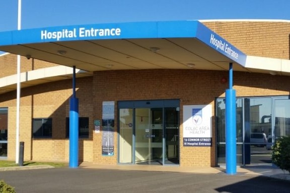 An exterior picture of a hospital with an orange brick exterior and a blue pillar and porch with Hospital Entrance written.