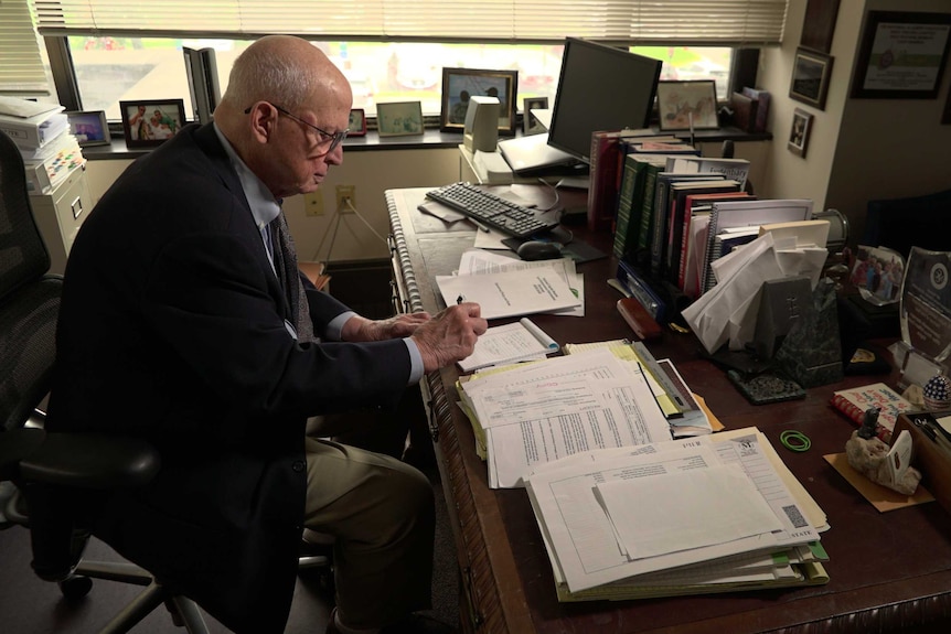 A man in a suit writing at a large desk