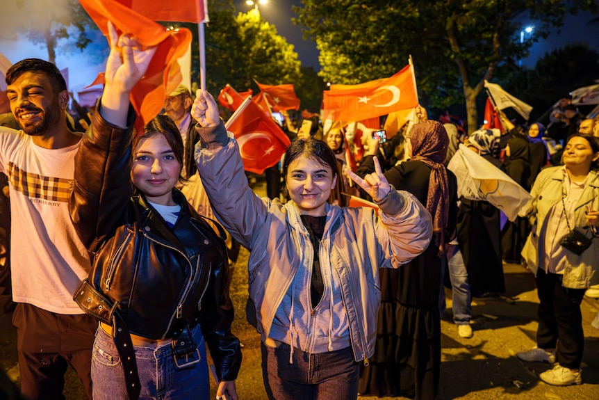 A girl gives a peace sign in a crowd of people 