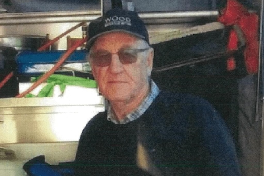 A man looks into he camera wearing a hat and standing in front of a van.