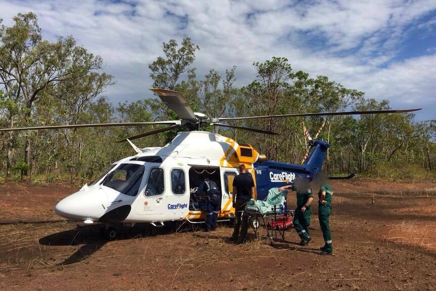 A careflight helicopter in bushland with paramedics getting a patient on board.