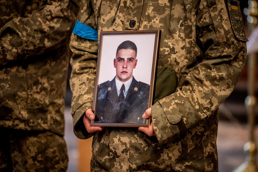A solider holds an image of Volodymyr next to his coffin.