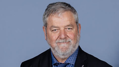 A head shot portrait of a male doctor with grey hair and a beard