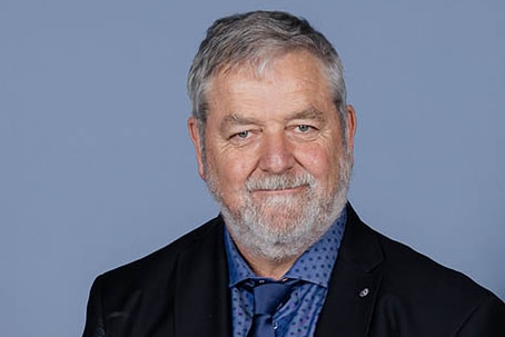 A head shot portrait of a male doctor with grey hair and a beard