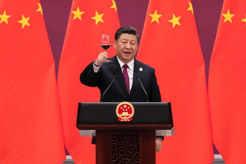 习近平站在九面大中国国旗前，站在官方讲师身后品尝一杯红酒。