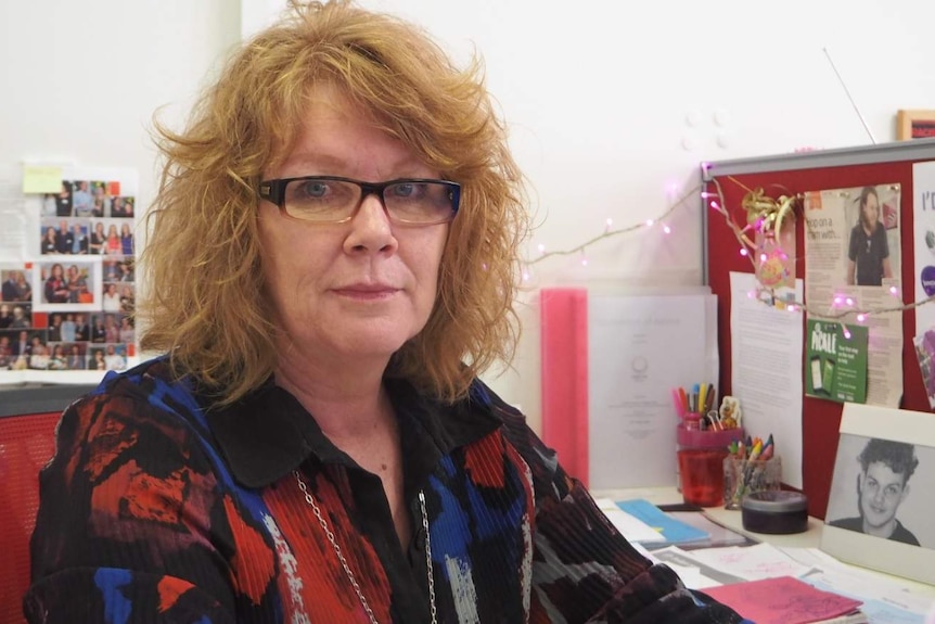 A woman with fluffy red hair and glasses looks at the camera.