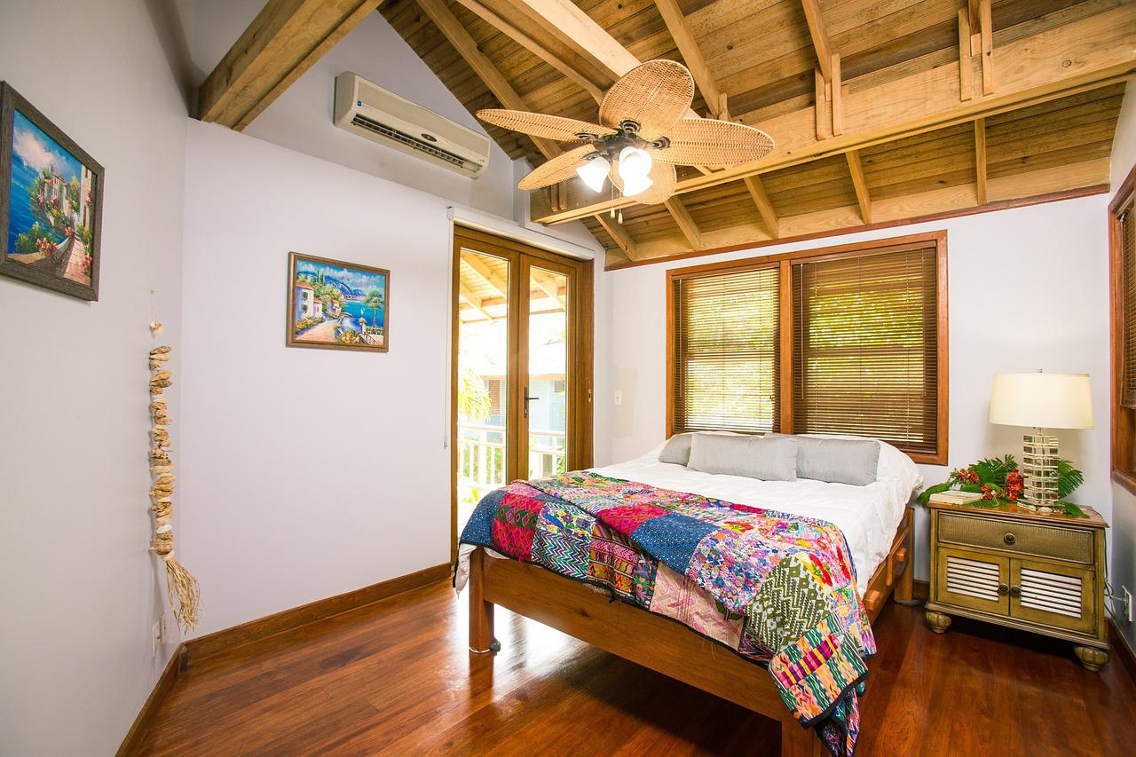 A bedroom in a beach house with timber ceilings and an overhead fan.
