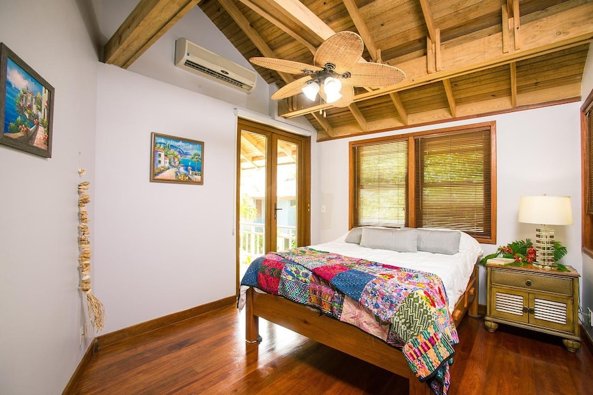 A bedroom in a beach house with timber ceilings and an overhead fan.