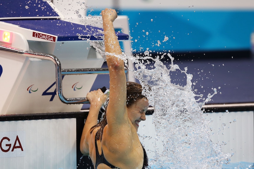Swimmer Ellie Cole raises her arm in the air in the pool in celebration.