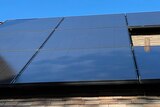 A worker places a solar panel on a roof next to those already in place.