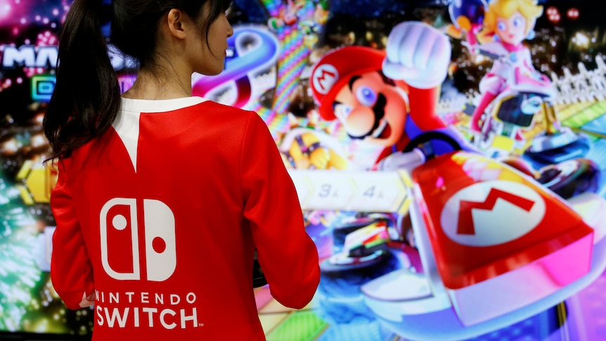 A woman wearing a read t-shirt with white lettering that says Nintendo Switch on the back.