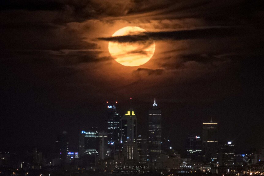 A supermoon with clouds in front of it sits over the Perth city skyline at night.