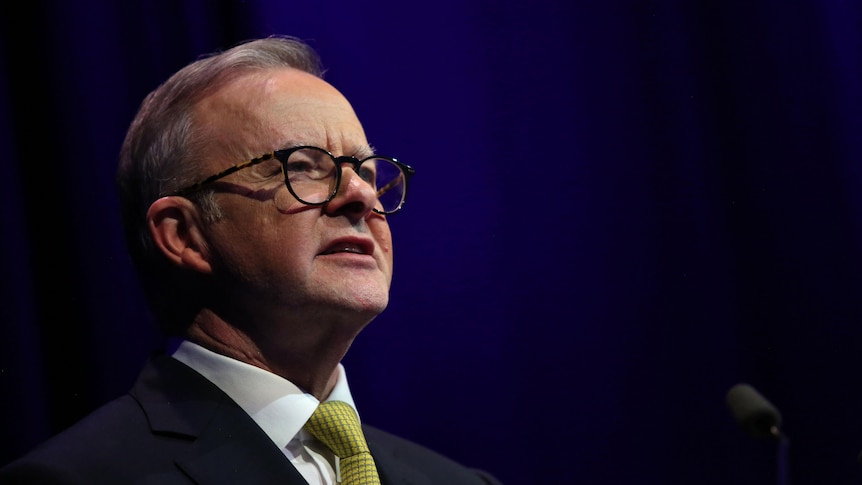 Anthony Albanese looks out to the audience, he wears a yellow tie with a suit