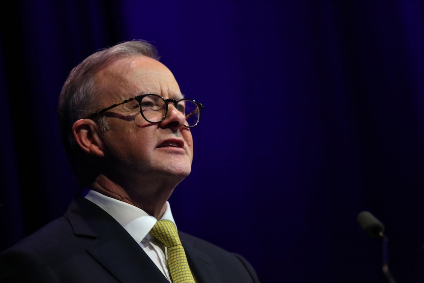 Anthony Albanese looks out to the audience, he wears a yellow tie with a suit