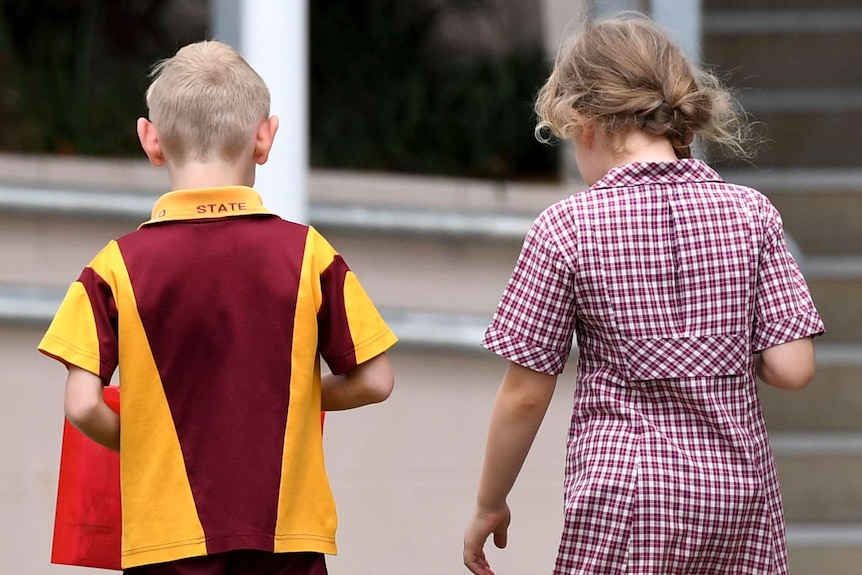 A boy and a girl in maroon, yellow and white school uniforms walk side by side outside.
