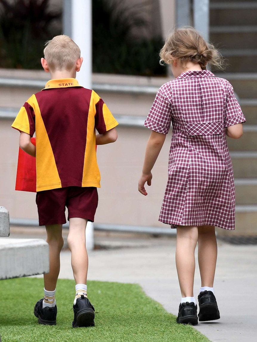 A boy and a girl in maroon, yellow and white school uniforms walk side by side outside.