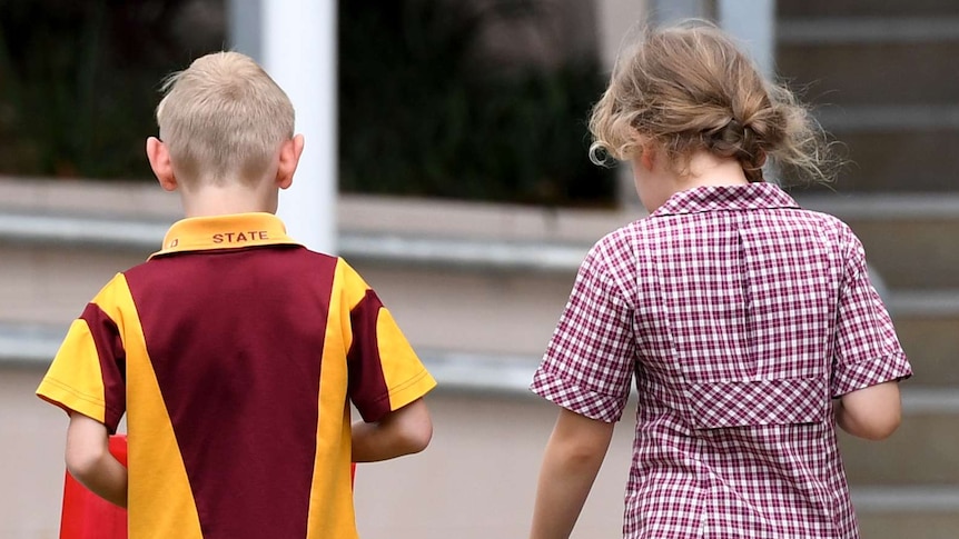 A boy and a girl in maroon, yellow and white school uniforms walk side by side outside.