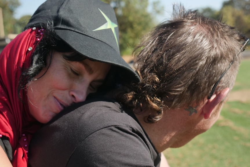 A woman hugs a man from behind. 