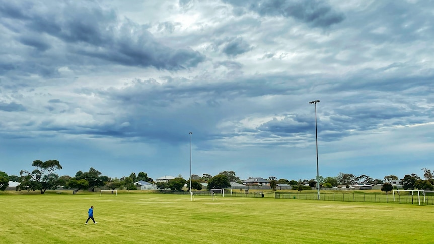 A person walks across a soccer field under grey skies