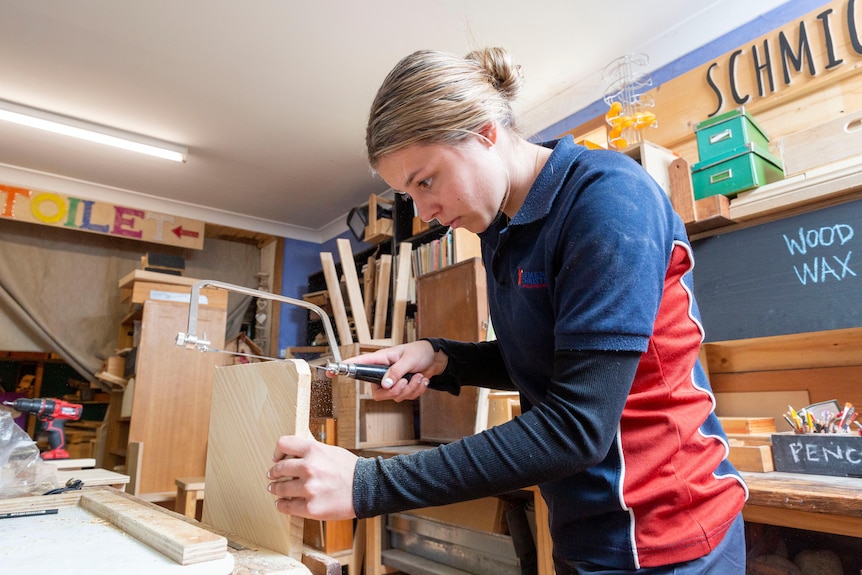 A teenage girl saws wood at a woodworking shed