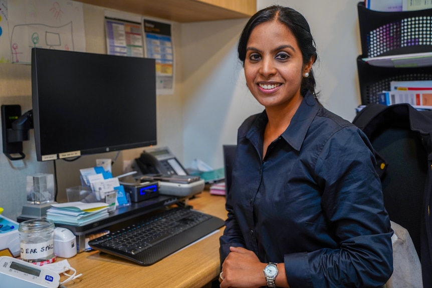 Dr Ramya Rama looking at the camera smiling while sitting at her work desk.
