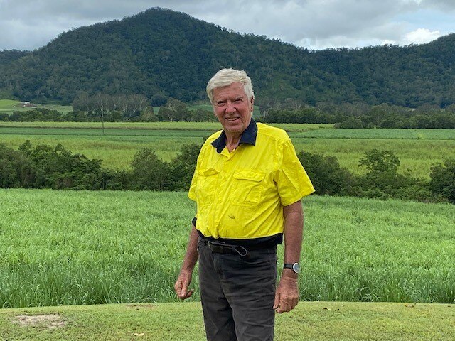 Farmer Bill Hobbs stands in front of a cane field, trees and other paddocks are visible in the background