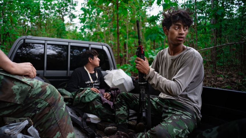 Armed rebels in the back of a pick up truck driving through a forest in Myanmar 