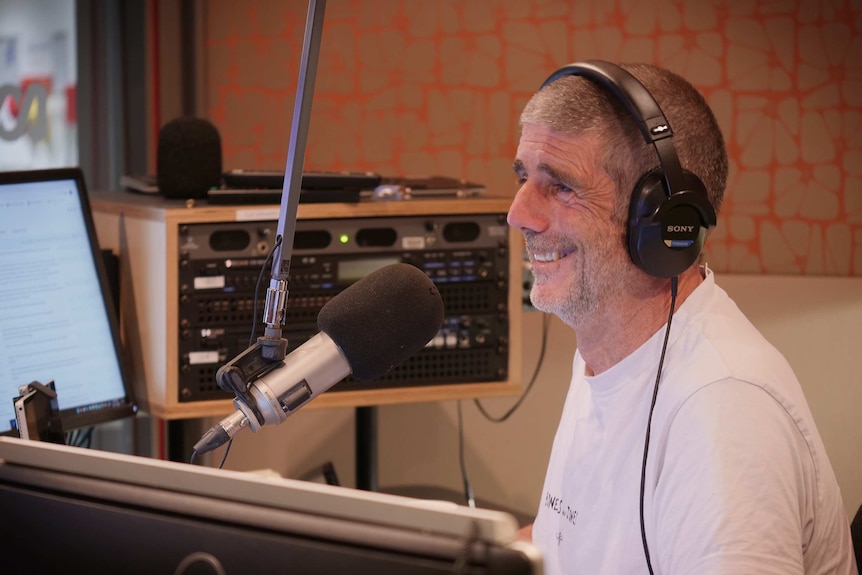 A man sits behind a microphone in a radio studio booth