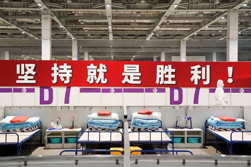 A worker in protective clothing walks past a banner reading "Persistence is victory!"