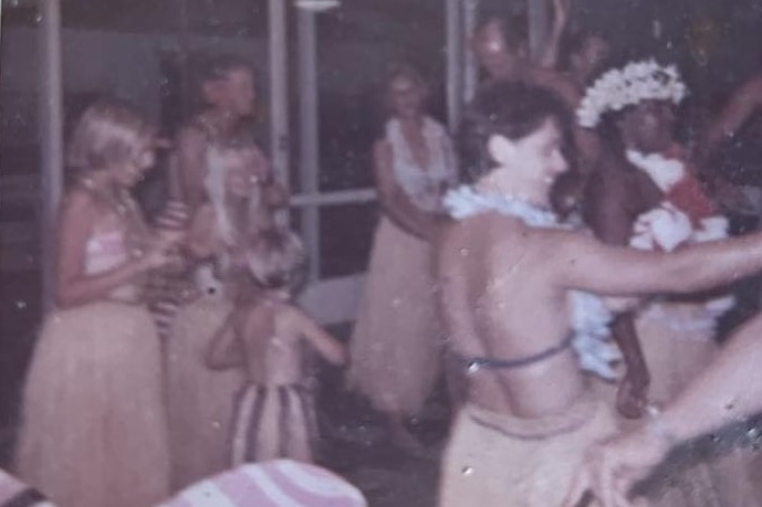 A Polaroid of a group of people hula dancing and smiling. 