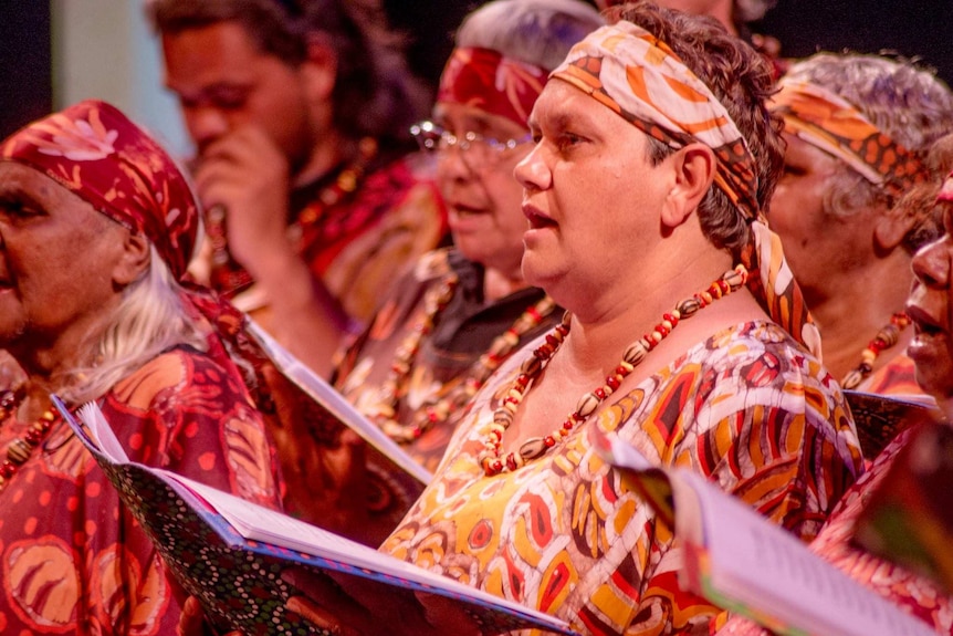 Women in colourful uniforms dance as a group holding folders