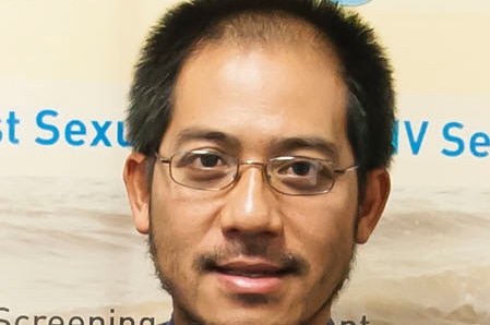 Clinical director of sexual health, Doctor Kuong Taing, smiling and standing in front of a sign.