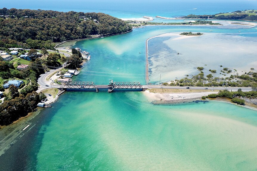 Narooma's Wagonga Inlet with bridge leading over bright blue water, as seen from the air.