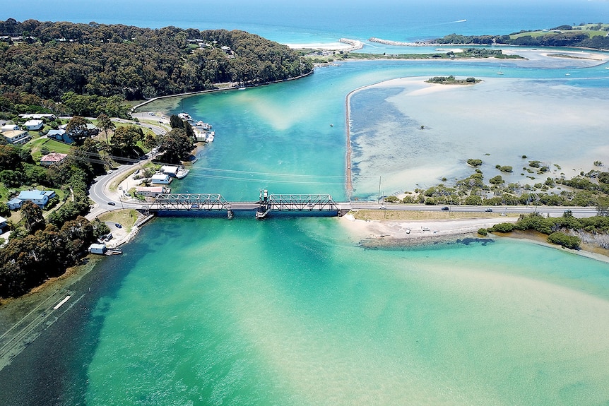 Narooma's Wagonga Inlet with bridge leading over bright blue water, as seen from the air.