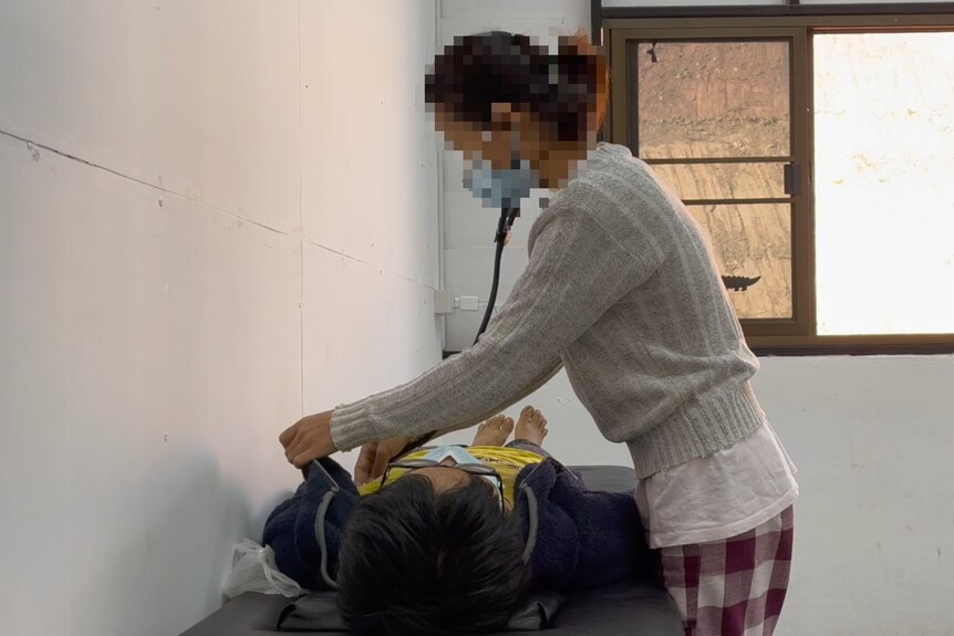A young doctor, whose face is pixelated to avoid identification, treats a patient laying on a bed.
