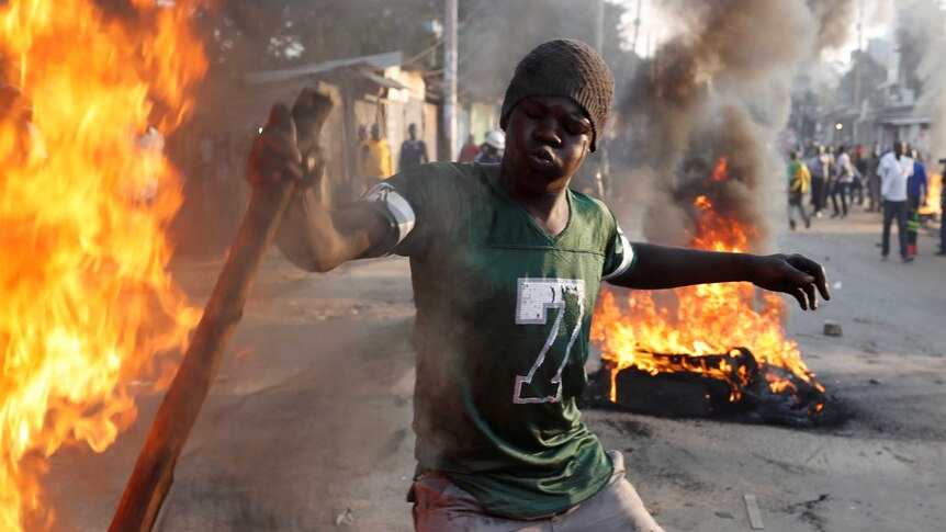 A man wields a stick as items burn in a street.