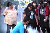 A group of five Indigenous people perform a smoking ceremony in the street of a regional town.