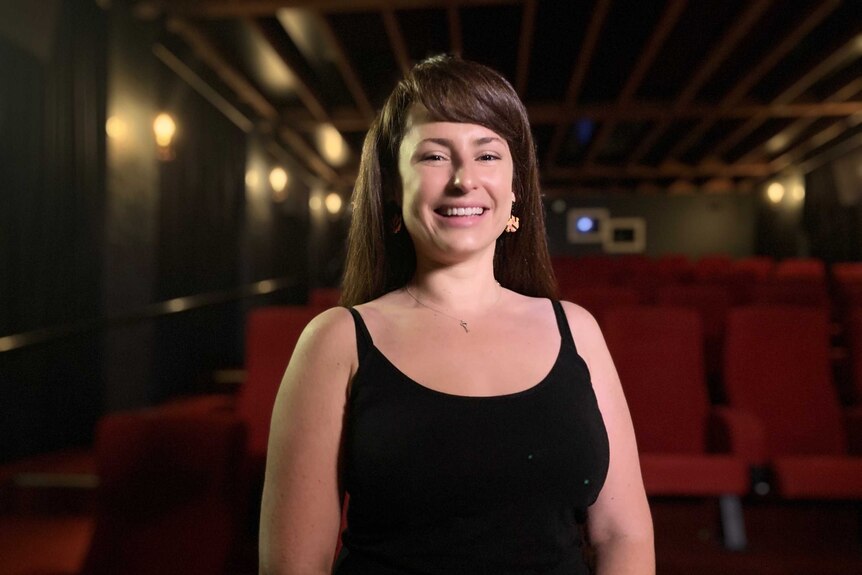 A woman stands in front of rows of empty cinema seats.