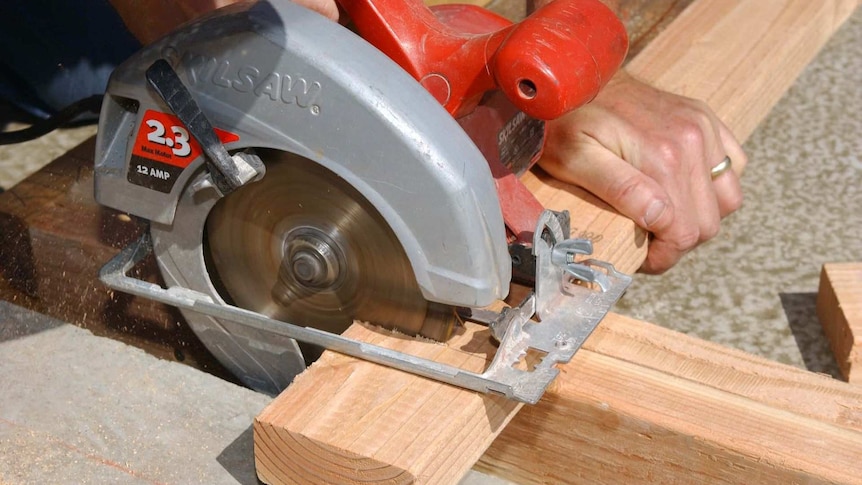 A man uses a circular saw to cut a plank of wood.