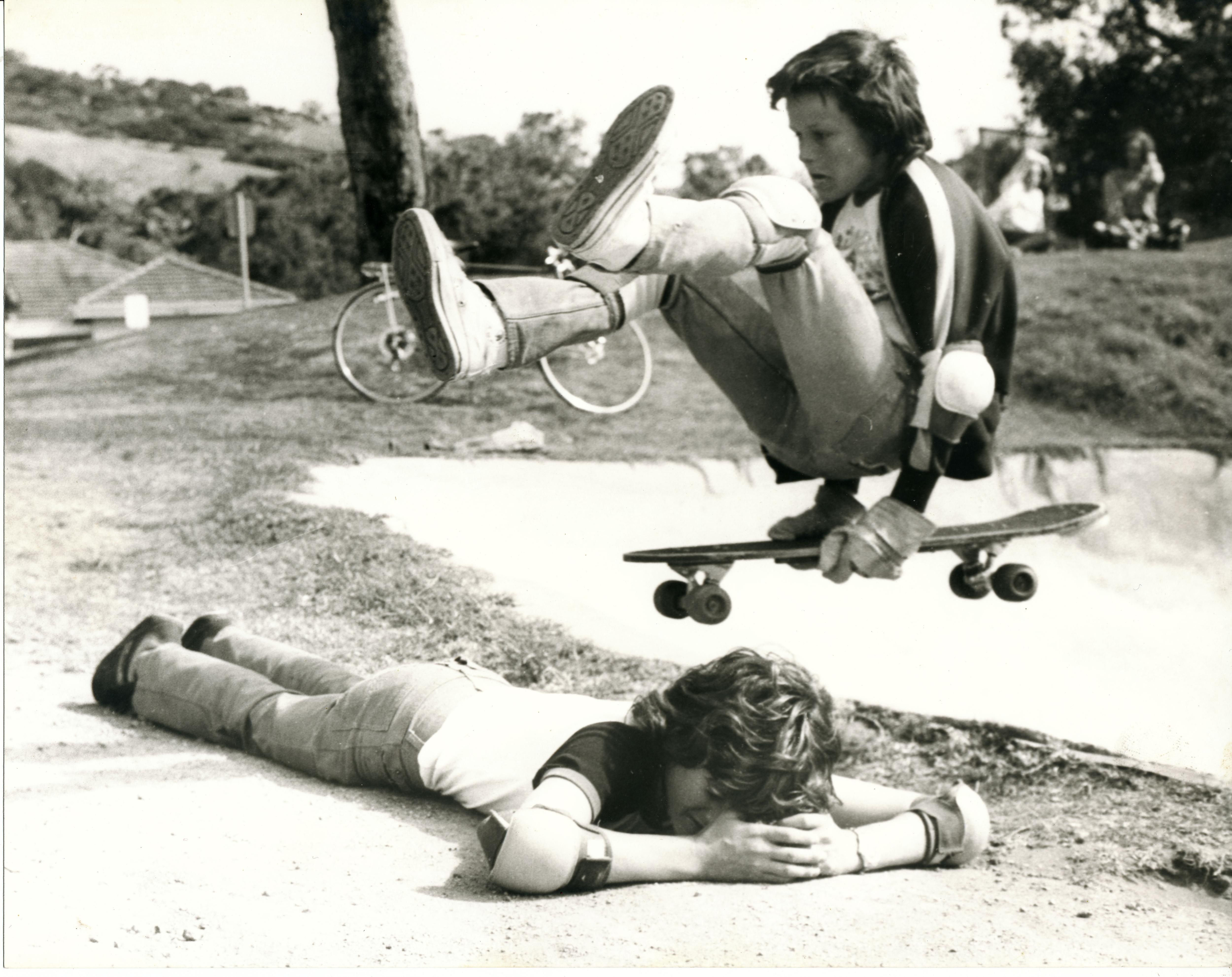 Un niño flota en una patineta sobre otro niño acostado.