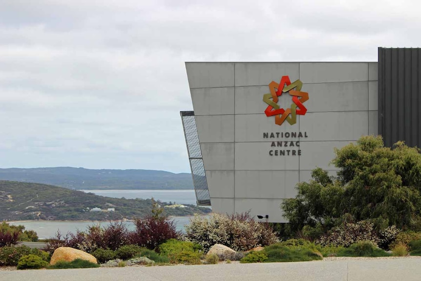 A grey building in front of a harbour surrounded by hills.