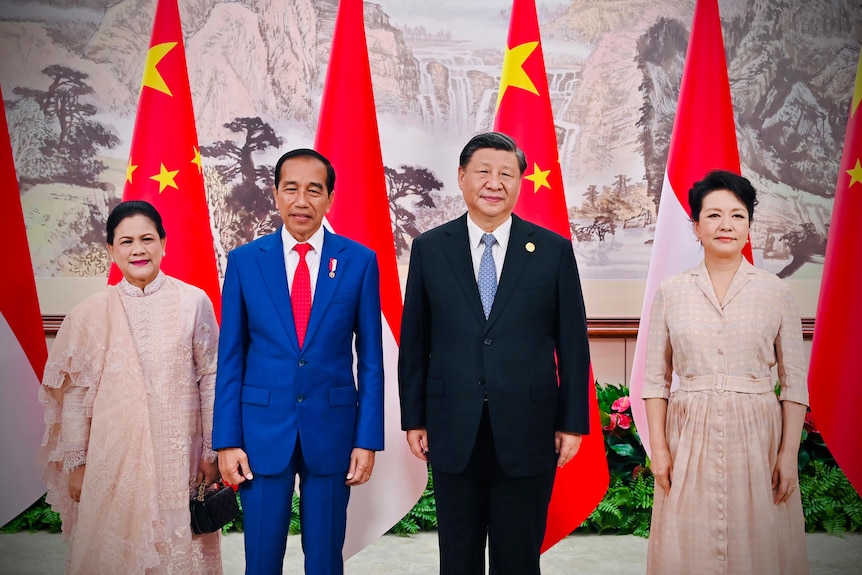 Joko Widodo and Xi Jinping, both wearing suits, smile standing alongside two women in front of Chinese and Indonesian flags. 