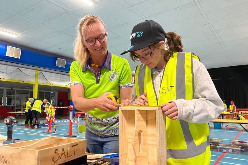 Two women with tools look over their woodwork 