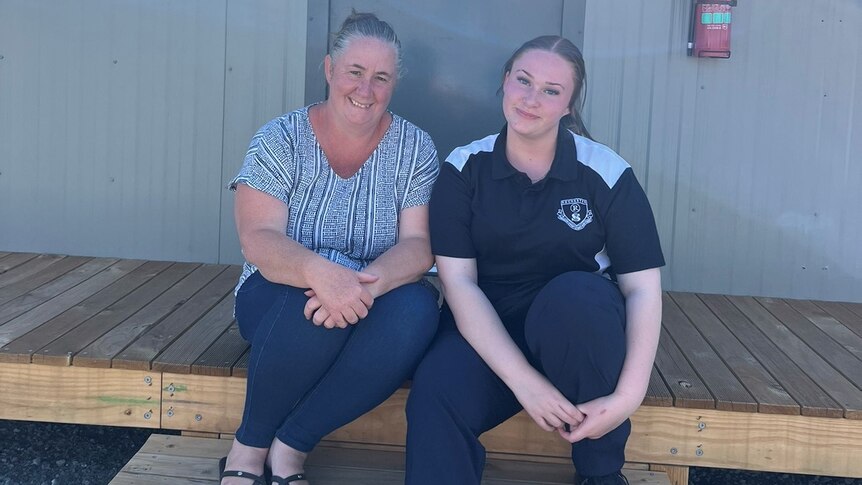 A woman and her teenage daughter sit on the steps of a cabin