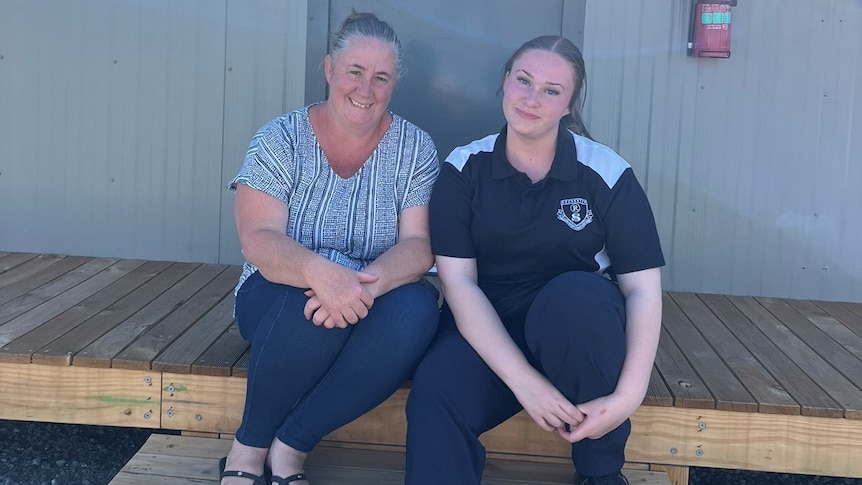 A woman and her teenage daughter sit on the steps of a cabin