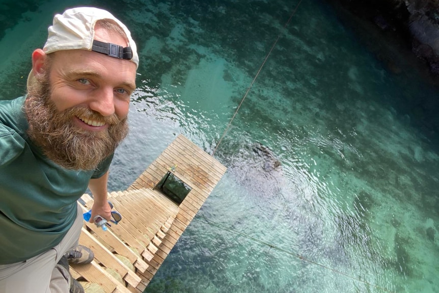 A man smiles at the top of a wooden ladder over turquoise water