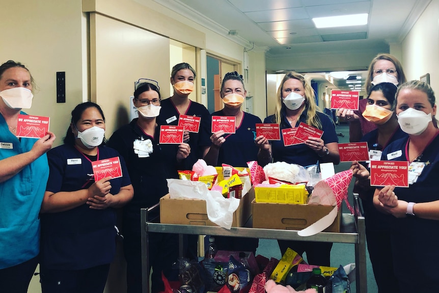 A group of medical staff wearing face masks hold up red cards around a trolley.