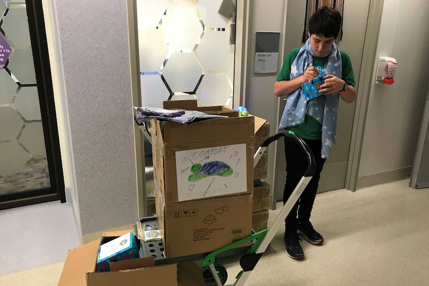 A boy writes on a card next to a trolley of gifts.