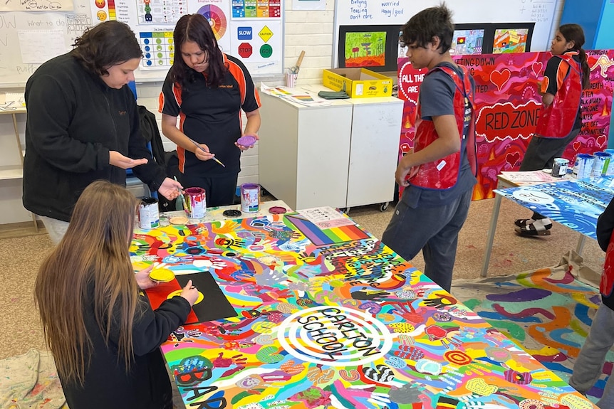 Five students in a classroom painting a collection of bright murals.
